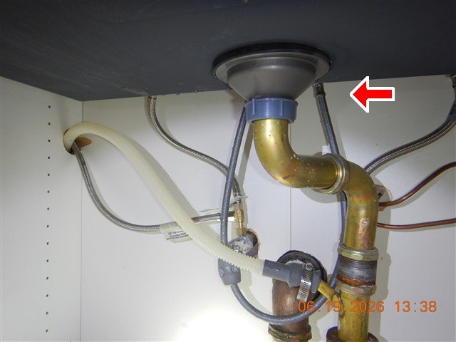 Under-sink brass trap and braided steel supply lines inside a cabinet, one connection arrowed.