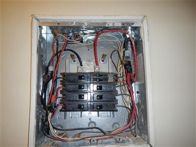 Open electrical panel with cover removed showing circuit breakers and red and black wiring