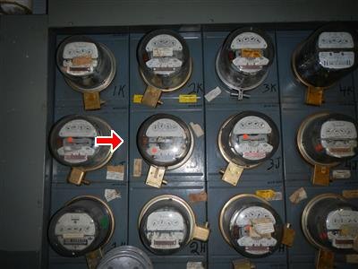 Rows of round glass electric meters on a gray board, red arrow marking one