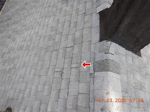Light-coloured roof shingles with a hairline crack arrowed and a dark patched area at the corner.