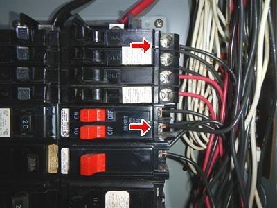 Close-up of panel breakers with two red arrows pointing at wire terminal connections