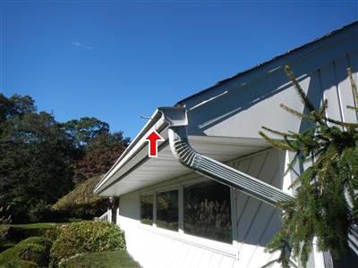 Aluminium gutter and downspout along the eave of a white house, red arrow at the gutter edge.