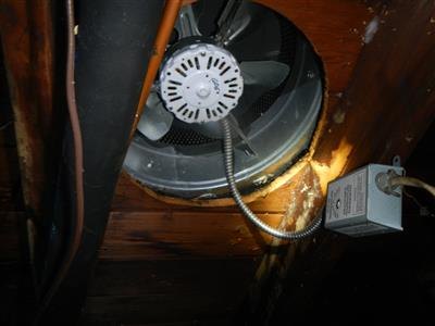 An attic exhaust fan mounted through the roof deck, with its flexible conduit and junction box.