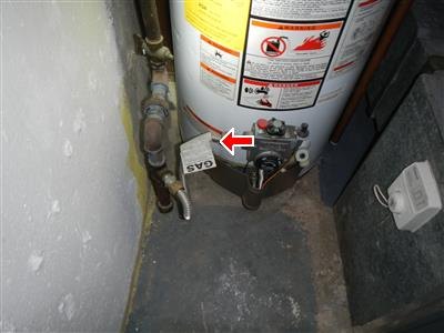 A gas water heater in a narrow utility closet, with an arrow at the gas control connection.