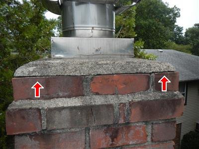 Brick chimney top with metal flue pipe and red arrows pointing at cracked mortar and concrete cap