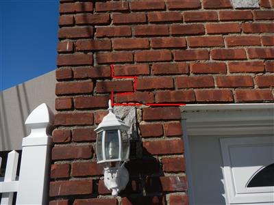 Red markup outlining a stepped crack in exterior brickwork above a garage door, next to a porch light