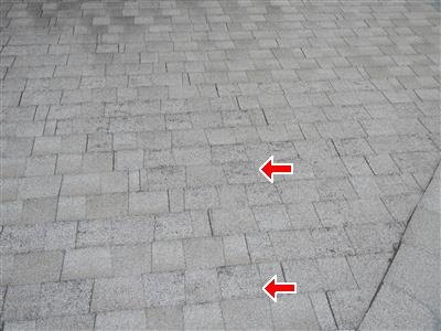 Gray asphalt shingle roof with two red arrows pointing at worn, darker patches