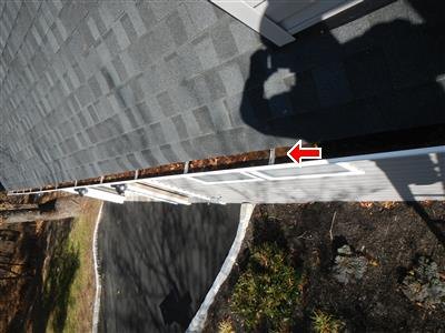 Looking down a roof edge at a rusted gutter, red arrow pointing at the corrosion