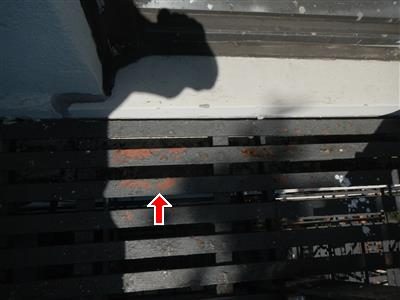 Steel fire escape slats with flaking paint and rust spots, red arrow pointing at the peeling area.