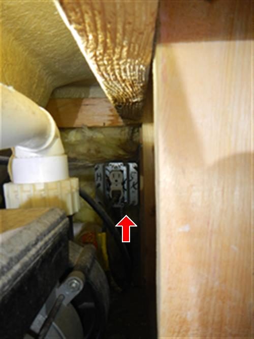 Wall outlet in a cramped space beside a tub pump and PVC pipe, red arrow pointing up at the outlet.
