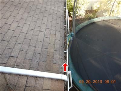 Gutter along a roof edge beside a trampoline, red arrow pointing to debris in the gutter.