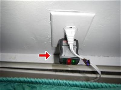 Plug-in outlet tester with coloured indicator lights in a wall receptacle, red arrow pointing at it.