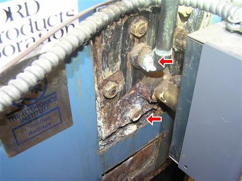Heavily corroded pipe fittings on the side of a boiler, two points arrowed.