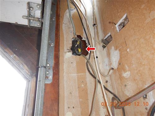 An open wall cavity beside a garage door frame with an exposed junction box arrowed.