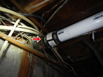 White PVC drain pipe running along a basement ceiling with a red arrow pointing at a coupling.