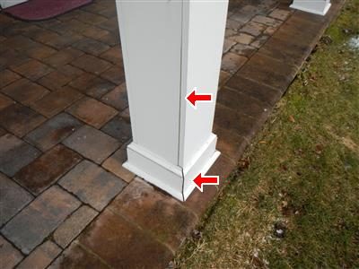 White porch support column base on brick pavers with two red arrows pointing at open corners in the moulding.