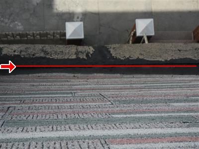 Flat roof edge meeting a brick parapet with a red line along the flashing seam, two vent caps behind.