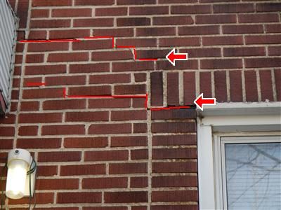 Brick wall above a window with stepped cracks traced in red and arrows at the lintel line.