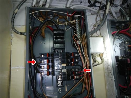 Open main electrical panel with breakers and wiring, two red arrows pointing at breaker terminals.