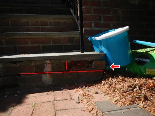 Brick cheek wall beside front steps with a horizontal crack marked by red lines and an arrow.