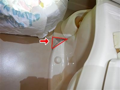 Base of a toilet on a tile floor with a red triangle outlining a gap where a tile is missing.