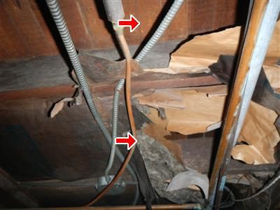Crawl space with kraft-faced insulation hanging down from between the floor joists, marked with two red arrows.