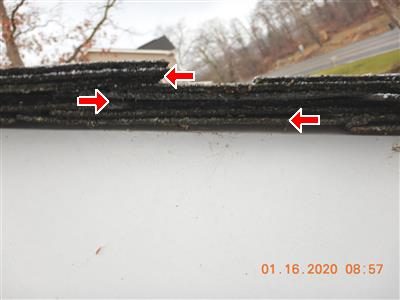 Edge of an asphalt roof seen from the gutter line with three stacked shingle layers marked by red arrows.