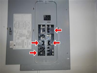 Closed grey electrical panel cover with four red arrows pointing at open knockout holes.